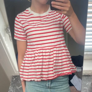 Randig topp från Zara - Supersöt topp från Zara i vitt med röda ränder. Toppen har korta ärmar, rund halsringning och en volangig nederdel som ger en avslappnad och trendig look. Den är använd ett fåtal gånger💞💞