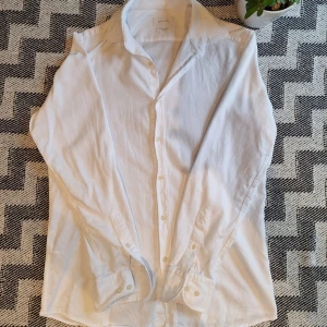 Vit skjorta från Massimo Dutti - Klassisk vit skjorta från Massimo Dutti i bomull med diskret struktur. Skjortan har använts bara ett par gånger. Skjortan har lång ärm, knappar i funktion och klassisk krage. Perfekt för en clean och stilren look. Snygg passform.