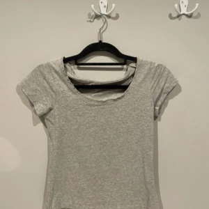 Grå basic topp från 157, XS - Enkel och stilren grå topp från 157 i storlek XS. T-shirten har rund halsringning och korta ärmar. Tillverkad i mjuk bomullsblandning med lite stretch för skön passform. Perfekt att matcha med jeans eller kjol för en clean look.