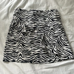 Zebramönstrad kortkjol från Lindex - Snygg kortkjol från Lindex med svartvitt zebramönster. Kjolen har resår i midjan för skön passform och är gjord i mjukt material. Säljer då den är för liten för mig men den är stor för att vara 146/152. Använd 2 gånger. Pris går att diskutera