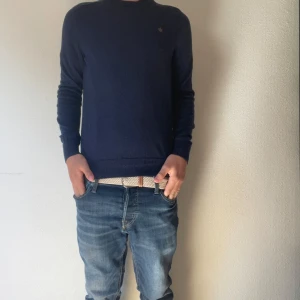 Mörkblå stickad tröja från Morris - Säljer en mörkblå stickad tröja från Morris med rund hals och diskret broderad logga på bröstet. Tröjan har lång ärm och klassisk passform, perfekt till jeans eller chinos. Materialet är mjukt och skönt mot huden.