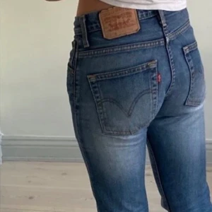 Levi's lowwaist bootcut jeans blå denim - Säljer ett par klassiska Levi's 527 jeans i blå denim. Modellen har låg midja och bootcut-ben, med snyggt slitna detaljer och femficksdesign. Jeansen har Levi's ikoniska läderpatch bak och röda logotag vid bakfickan. Perfekta för en avslappnad och cool look. Waist 27, längd 34
