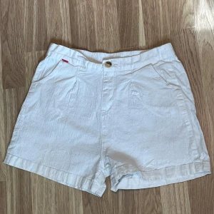 Vita shorts - Snygga vita shorts i bomull med avslappnad passform och klassisk midja. De har två fickor fram, knapp och dragkedja samt resår baktill för extra komfort. Perfekta för varma sommardagar och enkel att matcha med allt.