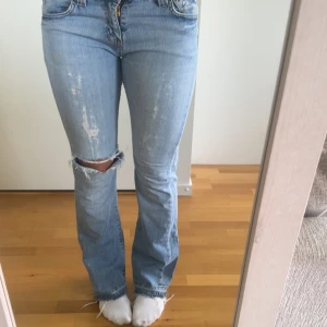 Ljusblå bootcut jeans med slitningar - Säljer ett par ljusblå bootcut jeans från lee med slitningar och hål på ena knät. Jeansen har klassisk femficksmodell, låg midja och råa kanter nertill. Perfekta för dig som gillar en avslappnad och trendig look.