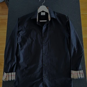  Burberry skjorta  - Snygg  stilren skjorta från Burberry med dem klassiska rutiga detaljer på insidan av kragen och ärmsluten. Skjortan är i storlek S men passar dig som bär M, knappar framtill och en stilren passform. Perfekt för dig som vill ha en unik look med lyxig känsla. Skjortan är köpt på Collage på NK för 6500. Använd 1 enda gång och allt og medföljer (kasse, extra knappar och kvitto) 