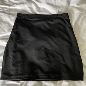 Svart tight kortkjol - Enkel och stilren svart kortkjol med tight passform. Kjolen är rak i modellen. Materialet känns mjukt och stretchigt.