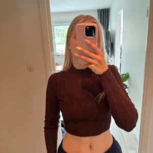 Brun croppad ribbad tröja NA-KD - Säljer en brun croppad långärmad tröja från NA-KD. Tröjan är ribbad med hög hals och har en tight passform som sitter snyggt på kroppen. Perfekt att styla med höga jeans eller kjol.