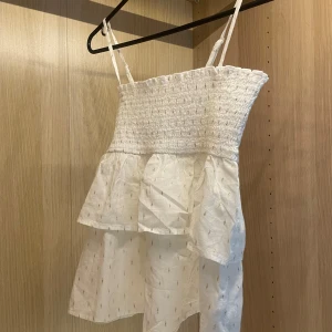 Vit volang linnetopp Gina Tricot - Supersöt vit linnetopp från Gina Tricot med smockad överdel och tunna axelband. Toppen har volanger och ett lätt, luftigt tyg med små broderade detaljer.