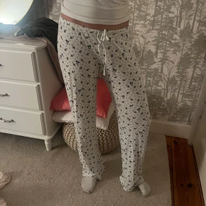 Vita mjukisbyxor med blått mönster NELLY - Supermysiga vita mjukisbyxor med blått småblommigt mönster och rosetter. Byxorna har snörning i midjan och är raka i modellen, perfekta för chill dagar hemma. Tillverkade i mjukt bomullstyg för extra komfort. Från Nelly.