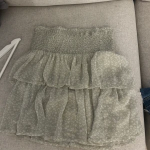 Ljusgrön volangkjol med smock - Supersöt ljusgrön kortkjol med smock i midjan och dubbla volanger. Kjolen har ett diskret mönster och är gjord i ett tunt, luftigt material som känns perfekt för varmare dagar.