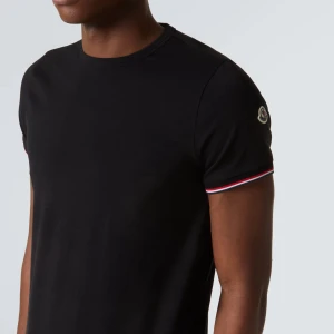 Svart Moncler t-shirt med logga - Svart t-shirt från Moncler i bomull med klassisk passform. Ärmarna har snygga rödvita detaljer och Moncler-logga på vänster ärm. Enkel och stilren design som passar perfekt till jeans eller shorts.