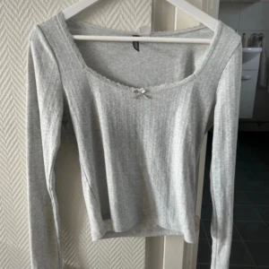 Ljusgrå pointelle topp med spets och rosett - Supersöt ljusgrå långärmad topp från H&M med pointelle mönster, spetskant vid urringningen och en liten rosett framtill. Mjuk och stretchig bomullsblandning som sitter skönt på kroppen. Knappt använd 💕 passar mig som är strl S