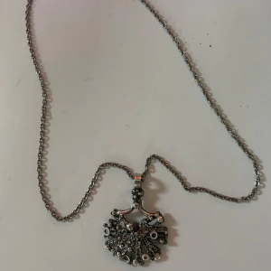 Unikt silverfärgat halsband med hänge - Ett coolt halsband i silverfärg med ett detaljerat, abstrakt hänge som har en organisk och lite industriell känsla. Kedjan är av klassisk modell och hänget har små kulor och kedjor som ger en edgy vibe. Perfekt för dig som gillar statement-smycken.
