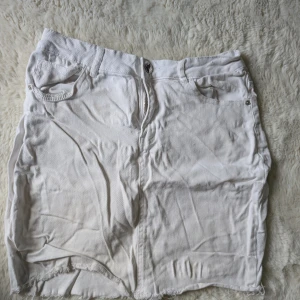 Vit jeanskjol från Amisu, strl 42 - Vit jeanskjol från Amisu i storlek 42. Kjolen har klassisk femficksdesign, dragkedja och knapp framtill samt rå, fransig nederkant för en avslappnad vibe. Perfekt till sneakers eller sandaler för en cool look.