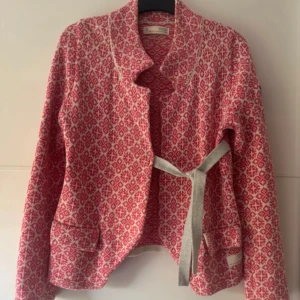 Odd Molly stickad cardigan jacka rosa - Odd Molly cardigan jacka i stickad ullblandning med rosa och vit mönster, broderad ros på ärmen och grått knytband i midjan. Långärmad och med snygga detaljer både fram och bak. Perfekt för dig som gillar unika plagg med coola broderier. Använd få gånger.