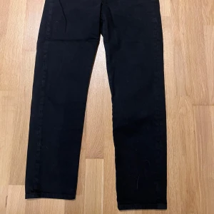 Svarta Levis jeans straight fit - Svarta jeans från Levis med klassisk röd logga vid bakfickan. Byxorna har rak passform och är tillverkade i ett mjukt bomullstyg. Strl: 26x27