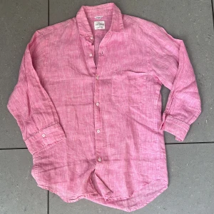 Rosa linneskjorta från Urban Research - Snygg rosa skjorta i 100% linne från Urban Research. Skjortan har klassisk krage, bröstficka och knäppning framtill. Perfekt för dig som gillar en avslappnad men ändå stilren look. (Obs! Skjortan har kortare armar, om man viker upp dem blir den as snygg.)
