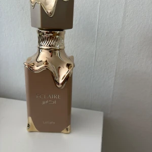 Lattafa Eclaire Eau de Parfum - Eclaire från Lattafa är en lyxig parfym i en beige och guldig flaska med unikt designad kork. Doften har söta toner av vanilj, karamell, honung och mjölkiga inslag. Perfekt för dig som gillar gourmanddofter och vill sticka ut med en elegant flaska i samlingen. Luktar som bianco latte. Endast testsprutad lådan har jag slängt, förvarad i svalt och mörkt ställe. Köpt för 3 mån sen. Nypris 449kr.
