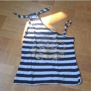 Offshoulder tröja   - Snygg svartvit randig oneshoulder topp från Heartquake med guldigt tryck framtill och fakeknyt på ena axeln. Barnstorlek men passar xs, eventuellt s.