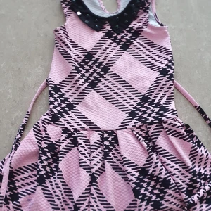 Klänning - Supersöt klänning i rosa med svart rutigt mönster och cool struktur. Klänningen har en svart krage med svarta nitar som ger en edgy touch. Materialet är stretchigt och känns bekvämt. Perfekt för dig som gillar att sticka ut med mönster och detaljer!