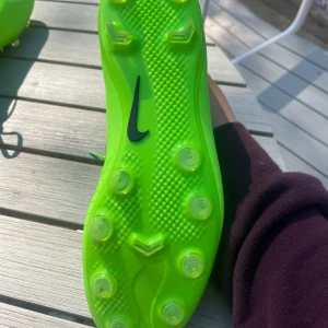 Veloce III fotbollskor - Säljer ett par riktigt snygga neongröna Nike fotbollsskor med svart swoosh. Skorna har hög strumpliknande krage, snörning och plastsula med dobbar för konstgräsplan. Ovandelen är i syntetmaterial och designen är slimmad för maxad bollkontroll. 