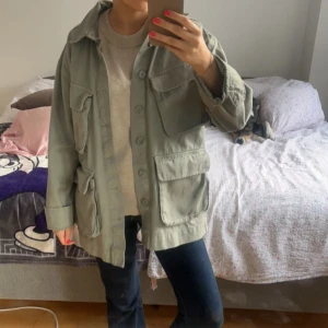 Ljusgrön jacka med stora fickor - Snygg ljusgrön overshirt med flera stora fickor framtill och knäppning med knappar. Jackan har en loose passform och är perfekt att slänga över en hoodie eller t-shirt. Enkel och stilren design som funkar till det mesta.