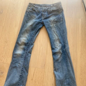 Miss Me blå bootcut jeans strl 27 - Säljer ett par blå jeans från Miss Me i klassisk bootcut-modell. Jeansen har snygga slitningar, kontrastsömmar och broderade detaljer på bakfickorna. Låg midja och coola nitar vid fickorna. Jag är 160 men dem är lite långa och skulle säga att de passar dig som har 34-38 i byx storlek. Kom även med prisförslag, har använt byxorna en gång för att de inte var min stil