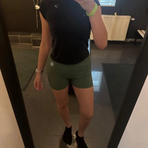 Gröna Gtech träningstights shorts - Snygga gröna träningstights shorts från Gtech med hög midja och tight passform. De är tillverkade i ett stretchigt syntetmaterial som sitter skönt och följer kroppen. Perfekta för gymmet eller löprundan, med diskret logga framtill och meshdetaljer på sidorna. Tyvärr lite luddiga i rumpan