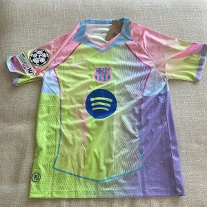FC Barcelona Lamine Yamal Nike tröja - Säljer en FC Barcelona fotbollströja med Lamine Yamal 10 på ryggen. Tröjan har coola pastellfärger i gult, rosa, lila och blått, med Nike-logga, Barca-emblem och Spotify-sponsor på bröstet. Korta ärmar och UEFA Foundation-märke på ärmen. Tillverkad i lätt och ventilerande material.
