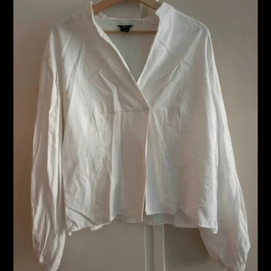 Vit långärmad skjorta med v-ringning - Säljer en stilren vit skjorta från Lindex med v-ringad hals och långärmade ärmar. Skjortan har en avslappnad passform och är tillverkad i mjuk bomull, perfekt för en clean och enkel look.