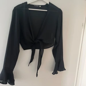 Svart bolero - Säljer en svart, bolero blus  H&M med långa ärmar och volang vid ärmsluten. Toppen knyts framtill och har en croppad passform som ger en trendig look. Perfekt att styla med höga jeans eller kjol.