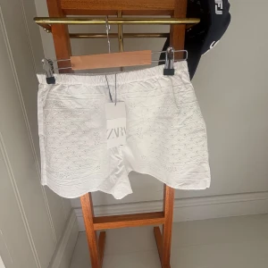 Vita broderade shorts från Zara XS - Snygga vita shorts från Zara i bomull med broderade detaljer framtill. De har elastisk midja och en avslappnad passform. Perfekta för varma dagar och ger en fräsch och somrig vibe.