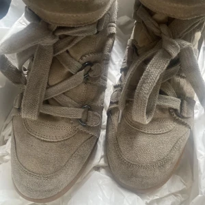 Beige sneakers med kilklack från Isabel Marant - Säljer ett par beigea sneakers från Isabel Marant i mocka med kilklack och bred snörning. Skorna har rund tå, platt gummisula och kardborreband upptill. Jättefina och matchar med massa outfits men säljer de för att jag sparar pengar till ett par andra skor. Kartong tillkommer.