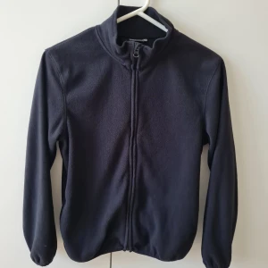 Fleecejacka från Cubus strl 152 - Mjuk och enkel svart fleecejacka från Cubus med dragkedja framtill och hög krage. Jackan har långa ärmar och är tillverkad i polyester. Storlek 152. Kan hämtas i Vallentuna.