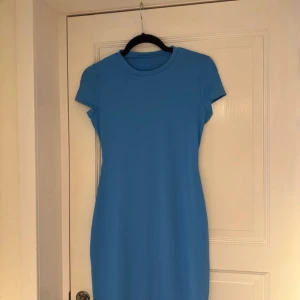 Blå långklänning med kort ärm - Enkel och stilren blå långklänning med rund halsringning och korta ärmar. Klänningen har en rak passform och är tillverkad i ett mjukt, stretchigt material som känns bekvämt mot huden. Perfekt för dig som gillar minimalistisk och clean stil.