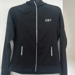 Svart träningsjacka från OTP med huva - Svart träningsjacka från OTP, med hel dragkedja framtill och huva. Jackan har reflekterande detaljer på fickor och axel. Storlek M, men passar även om man har storlek S. Aldrig använd. 