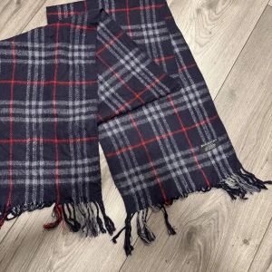 Rutig mörkblå halsduk från Burberry - Pris går alltid att diskutera, skicka gärna ett bud!     Snygg halsduk från Burberry i mörkblått med klassiskt rutigt mönster i grått och rött. Gjord i 100% kashmir för en lyxig och mjuk känsla. Halsduken har fransar i ändarna och passar perfekt för kalla dagar.