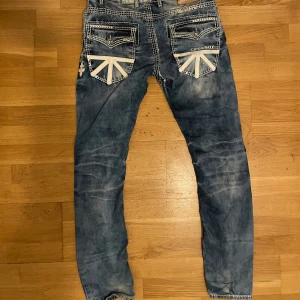 Cipo & Baxx blå jeans med detaljer - Säljer ett par blå jeans från Cipo & Baxx med coola slitningar, kontrastsömmar och unika vita detaljer på bakfickorna. Jeansen har raka ben och är tillverkade i 100% bomull. Perfekta för dig som gillar streetstyle och vill sticka ut.  Kontakta mig vid minsta fundering 