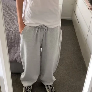 Gråa loose fit mjukisbyxor med snörning - Säljer ett par baggy joggers från Bershka. De är väldigt baggy och super sköna. Har snören så man kan justera midjan, fickor på sidorna och en på baksidan och är justerbar vid benen. Storlek XS men sitter som S/M (Inte mina bilder)