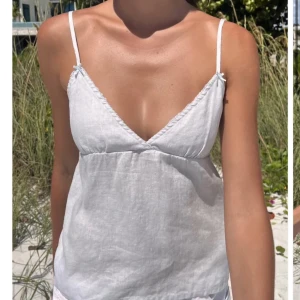 Vit linnetopp med smala axelband - Superfin vit linnetopp med smala justerbara axelband och v-ringning. Toppen har en feminin passform med knyt i ryggen och är tillverkad i svalt linne – perfekt för varma dagar. Enkel och stilren design som passar till allt.