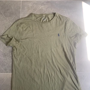 Äkta polo Ralph Laurent tröja - T-shirt från Ralph Lauren – militärgrön (storlek M) Snygg och stilren T-shirt från Polo Ralph Lauren i en tidlös militärgrön färg. Ikoniska loggan broderad på bröstet i marinblått. Modellen är i 100 % bomull – mjuk, bekväm och perfekt för både vardag och avslappnade outfits.  ✔️ Äkta vara ✔️ Skön passform ✔️ Lätt att matcha ✔️ Diskret och stilren  Lite skrynklig på bilden men i fint skick – inga hål eller fläckar! Nypris ca 400–500 kr. Säljer för endast 150 kr! 🔥  Skicka gärna meddelande vid frågor!