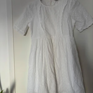 Vit broderad sommarklänning i bomull - Superfin vit klänning i bomull med broderade blommor och spetsdetaljer. Modellen är kortärmad med rund hals och har en lätt utställd kjol. Perfekt för varma dagar och har en romantisk, söt känsla med sina broderier och spetskanter.