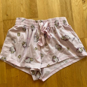 Hello Kitty rosa pyjamas shorts med snörning - Supergulliga rosa shorts från Hello Kitty med tryck av Hello Kitty och nallebjörnar över hela tyget. De har elastisk midja och en söt rosett framtill. Den har inga defekter och har använts ett fåtal gånger.