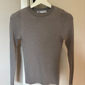 Ribbad grå långärmad tröja Zara - Supersnygg ribbad långärmad tröja från Zara. Tröjan har rund halsringning och är figurnära med stretchigt material och tyget är tunt vilket gör att den är lätt genomskinlig 