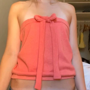 Korallrosa bandeau tubtopp med rosett - Superfin bandeau tubtopp i korallrosa med en söt rosett framtill. Toppen är axelbandslös och har en avslappnad passform, perfekt för varma dagar. Mjuk och skön känsla, enkel att styla till jeans eller kjol. Öppen att diskutera pris