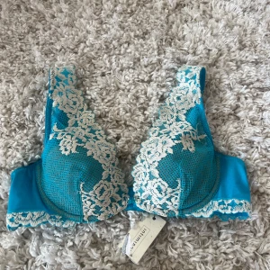 Intimissmi bh helt ny - Supersnygg turkos linnetopp med vita spetsdetaljer och blommigt mönster längs kanterna och axelbanden. Toppen har vadderade kupor och tunna axelband, perfekt för att ge en feminin och fräsch look. Materialet är mjukt och följsamt. Aldrig använd!!