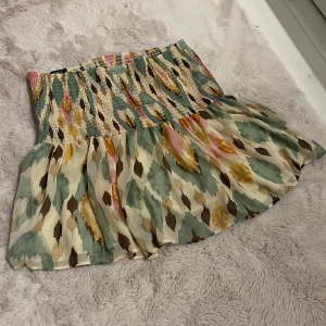 Mönstrad kortkjol - Superfin kortkjol från Lindex  med färgglatt mönster i grönt, beige, rosa och brunt. Kjolen har smock i midjan och ett flowy, volangigt fall. 