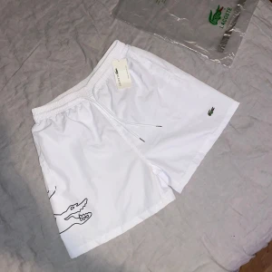 Vita Lacoste badshorts  - Hej!👋🏽 Jag säljer mina Vita shorts från Lacoste i storlek M/L.  Shortsen är helt oanvända och är i ny skick👌🏼. Hör självklart av dig om du har någon fundering eller fråga😊