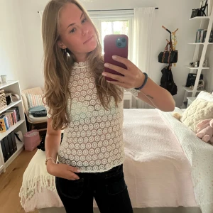 Vit spetsblus med cirkelmönster - Superfin vit blus i spets med unikt cirkelmönster och korta ärmar. Hög hals med vågig kant och knapp i nacken. Blusen är lätt genomskinlig och har en feminin, lite figurnära passform. Perfekt för dig som gillar detaljer och romantisk stil.