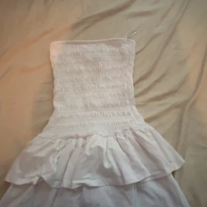 Vit kort klänning från Gina Tricot - Supersöt vit kort klänning från Gina Tricot med smockad överdel och volangig kjol. Axelbandslös modell. Andvänd 1 gång. 